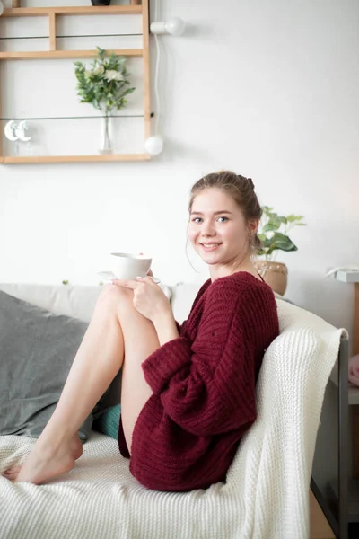 快乐的女孩坐在沙发上, 喝着清晨的热咖啡。. — 图库照片