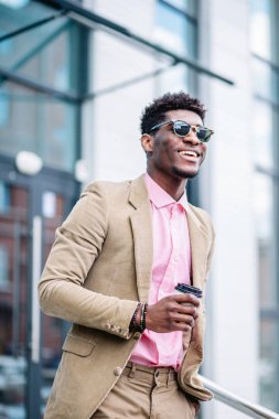 Neşeli siyah tenli adam sokakta plastik bir fincan kahve tutuyor.