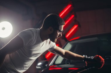 Araba temizliği. Adam mikrofiberi elinde tutuyor ve arabayı cilalıyor.