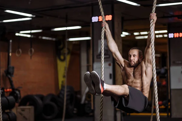 Male gymnast is trying to perform the exercise on ropes — Stock Photo, Image