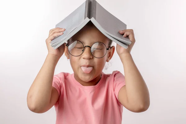 Смешная девушка с книгой на голове показывает свой язык — стоковое фото
