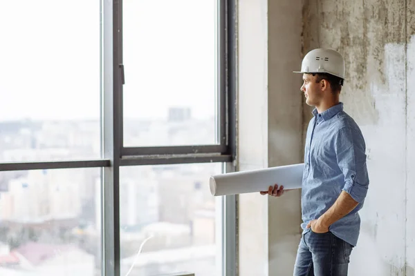 Stilig kille i hardhat att sätta sin hand på fickan och titta på fönstret — Stockfoto