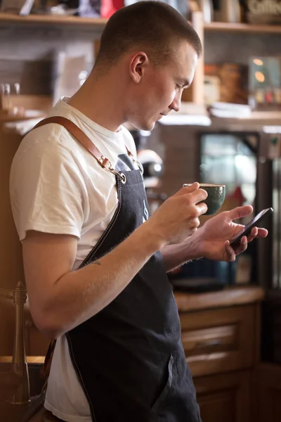 Pleasant waiter is looking at the screen of the cell phone. surf the net. — Stock Photo, Image