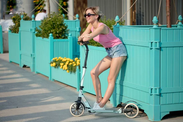 Beautiful girl poising in summer in city and next to blue kick scooter — Stock Photo, Image