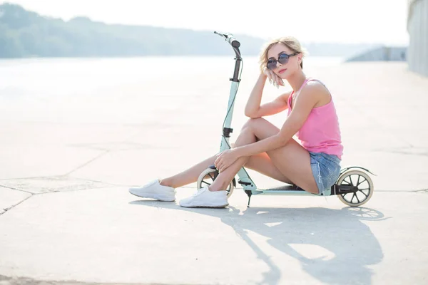 Mujer rubia positiva sentada en el patinete scooter azul — Foto de Stock