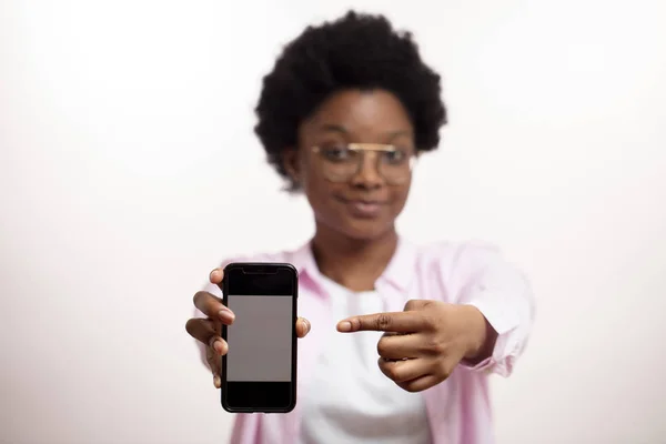 Olhe aqui por favor. Mulher sorridente agradável anunciando um telefone inteligente na moda — Fotografia de Stock