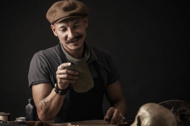 Bıyıklı ayakkabıcı atölyedeki masada ölçüm yapıyor.