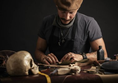 Bıyıklı ayakkabıcı atölyedeki masada ölçüm yapıyor.