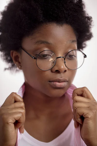 afro woman in glasses looking aside and holding the collar of a shirt
