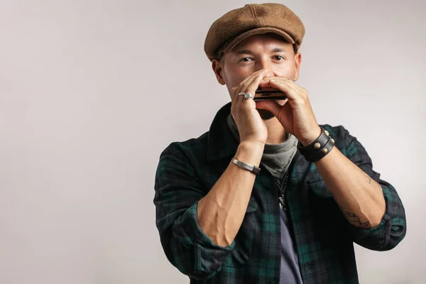 Studio portrait of caucasian moustached man on cap playing harmonica — Stock Photo, Image