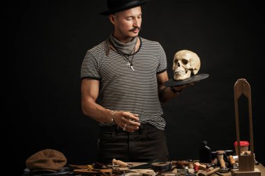 Bıyıklı, şapkalı, kafasında kafatası olan şık bir adam.