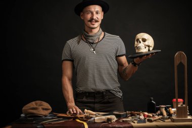 Bıyıklı, şapkalı, kafasında kafatası olan şık bir adam.