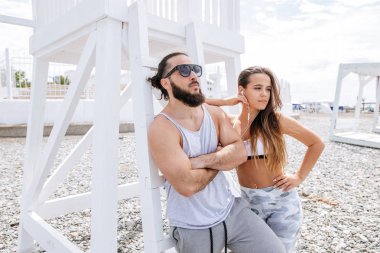 Genç çift, çakıl taşlı plajda dinlenirken kulaklıkla müzik dinliyor.