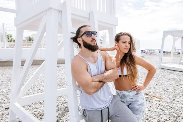 Genç çift, çakıl taşlı plajda dinlenirken kulaklıkla müzik dinliyor.