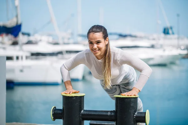Спортивная женщина тренируется на открытом воздухе, занимаясь кроссфитом на океанском пирсе. — стоковое фото