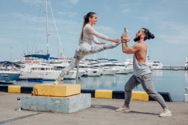 Erkek koç, iskelede egzersiz yapan genç kadına yardım ediyor..