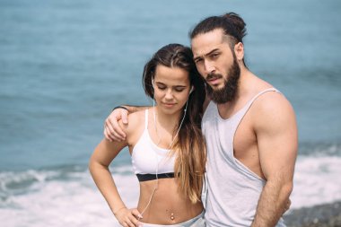 Yaz sabahı kumsalda sarılan bir çift ve arka planda deniz kölesi.