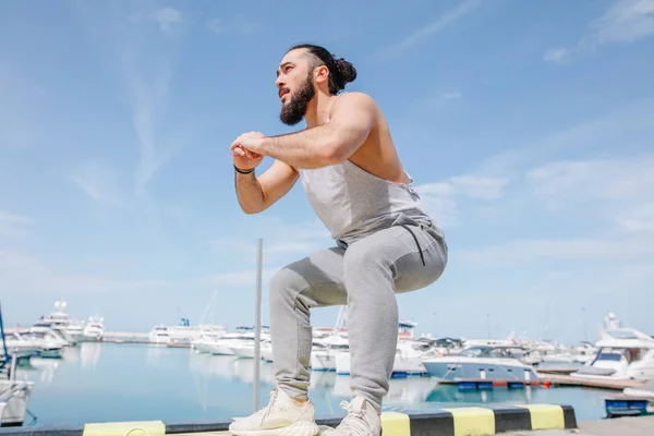 Fitness athlete doing jump squats on makeshift plyo-box on summer sea pier