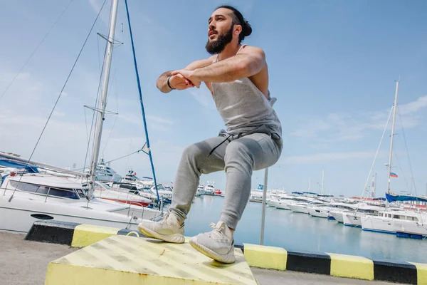 Fitness athlete doing jump squats on makeshift plyo-box on summer sea pier