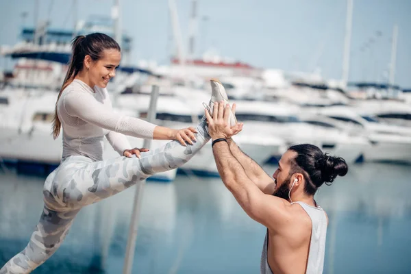 Muž trenér pomáhá mladé ženě cvičení na molu. — Stock fotografie