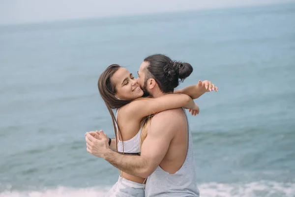 Couple cuddling on beach in summer morning with the sea serf on background — Stock Photo, Image