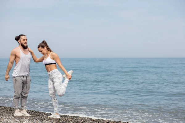 Pareja deportiva calentándose, estirando las piernas juntas en una playa — Foto de Stock