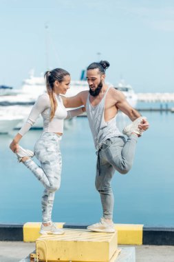 Genç ve güzel bir çift okyanus rıhtımında esneme egzersizleri yapıyor.