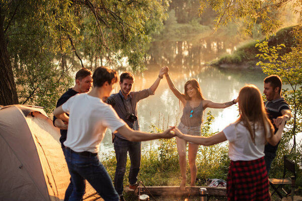 young positive people dancing around the campfire.