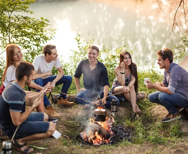 Gruppo di amici sono seduti intorno al fuoco del campo e la preparazione di salsicce . — Foto Stock