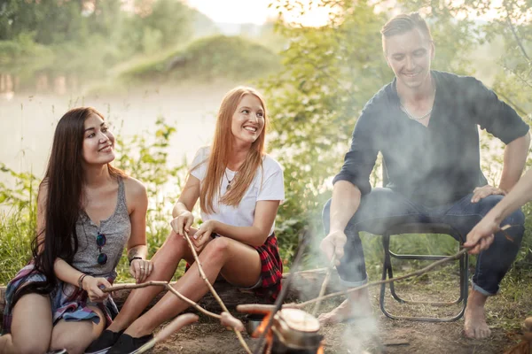 Ragazze allegre e ragazzo piacevole stanno cucinando sul falò — Foto Stock