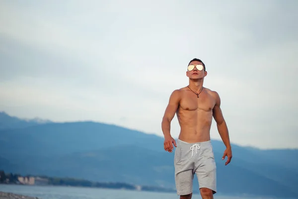 Homem de corpo masculino em óculos de sol na praia com mountauns no fundo — Fotografia de Stock