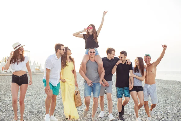 Grupo de amigos caminando en la playa, divertirse, las mujeres a cuestas en los hombres, vacaciones divertidas — Foto de Stock