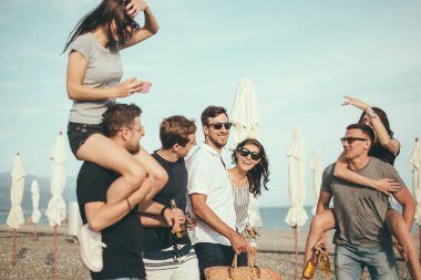 Bir grup arkadaş sahilde yürüyor, eğleniyor, kadınlar erkekleri sırtında taşıyor, komik bir tatil.