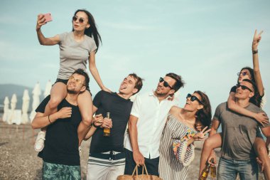 Bir grup arkadaş sahilde yürüyor, eğleniyor, kadınlar erkekleri sırtında taşıyor, komik bir tatil.