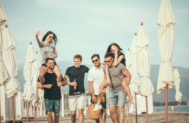 Bir grup arkadaş sahilde yürüyor, eğleniyor, kadınlar erkekleri sırtında taşıyor, komik bir tatil.