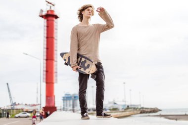 Tarz sahibi bir adam sokakta durur ve uzun tahtayı elinde tutar.