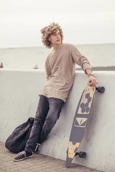 Mannelijke uitziende kant met t-shirt houten longboard houden tegen de betonnen muur — Stockfoto