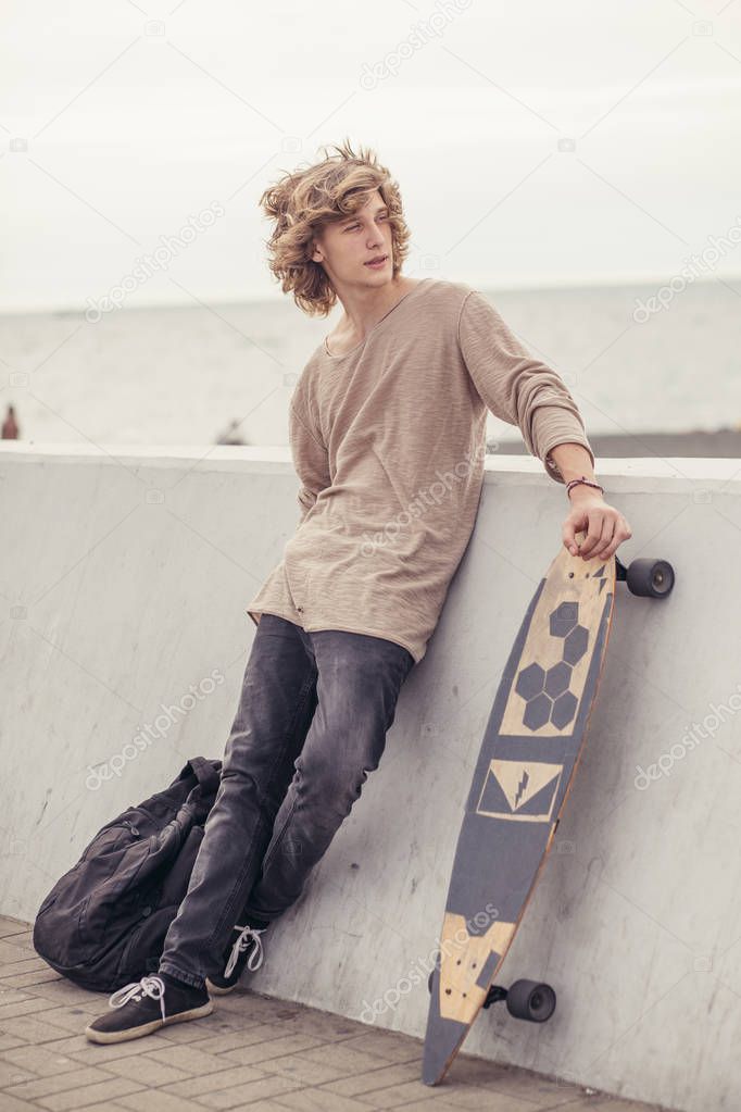 male looking side wearing t-shirt holding wooden longboard against concrete wall