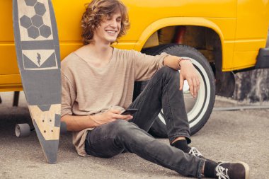 telefonunu kullanarak longboard üzerinde oturan hipster adam