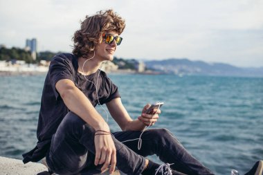 telefonunu kullanarak longboard üzerinde oturan hipster adam