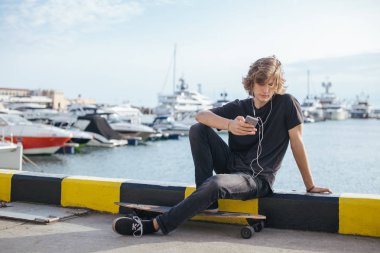 telefonunu kullanarak longboard üzerinde oturan hipster adam