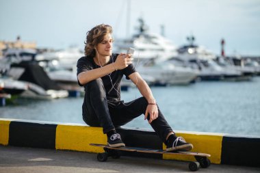 telefonunu kullanarak longboard üzerinde oturan hipster adam