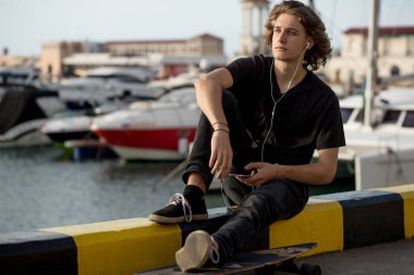 telefonunu kullanarak longboard üzerinde oturan hipster adam