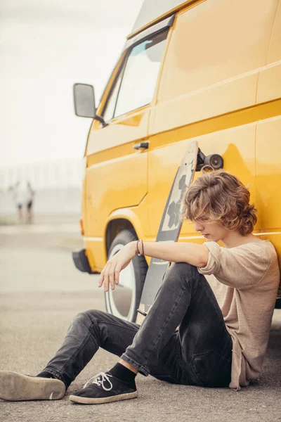 Hipster chico sentado al lado de su coche amarillo durante el viaje por carretera — Foto de Stock