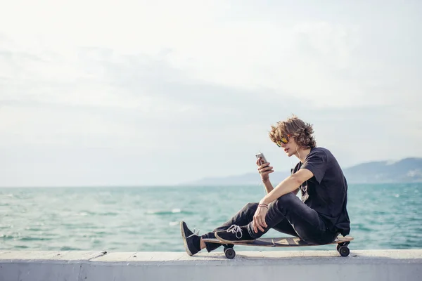Hipster man sitting on longboard using his phone — Stock Photo, Image
