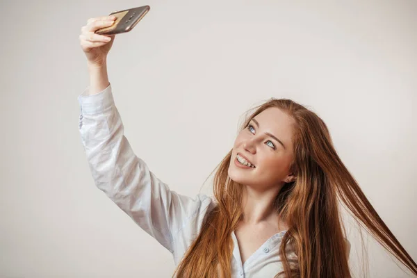 Joven emocional atractiva pelirroja femenina sosteniendo teléfono inteligente aislado en el estudio — Foto de Stock