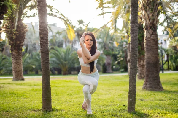身穿白色运动服、表演瑜伽鹰的女人站在公园草地上的室外. — 图库照片