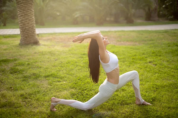 Woman practicing Warrior yoga pose outdoors over green nature background.