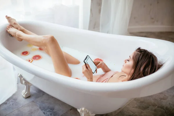 自宅で風呂に入りながら携帯電話を使う可愛い女性は — ストック写真