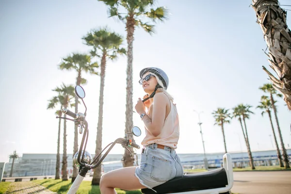 Молодая девушка в шлеме и защитных очках сидит рядом с электрическим велосипедом — стоковое фото
